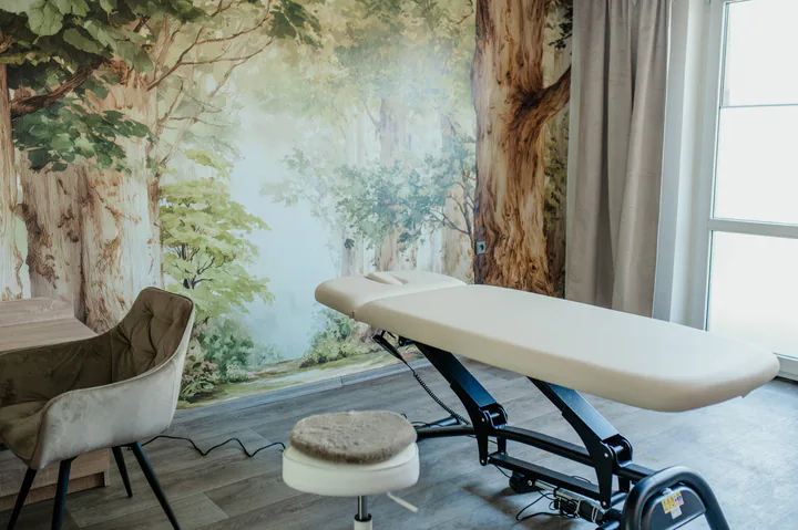 Světlá ordinace DOSIA fyzio CARE s lesní tapetou a terapeutickým lehátkem